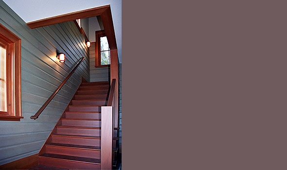 Wooden staircase with horizontal siding wall and wall-mounted sconces.