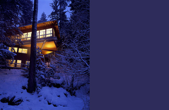 Cascade Lake House shows warm interior lighting through large windows amid snow-covered trees at dusk.