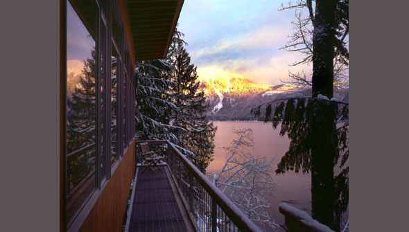Narrow balcony with metal railing faces a snowy lake and mountain view at sunset.