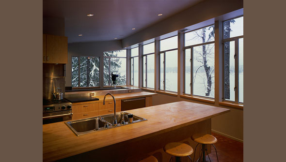Kitchen at Cascade Lake House features wood countertops and expansive windows with lake views amid snow-laden trees.