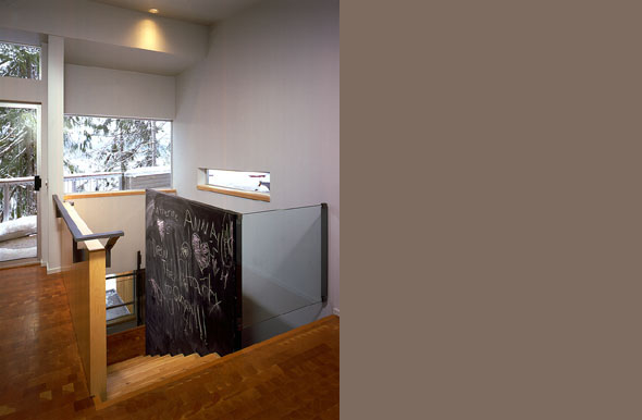 Cascade Lake House stair area with wood flooring and glass panel railing looking out to snowy trees in Seattle.