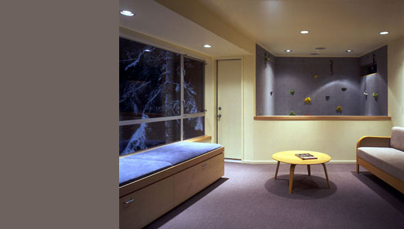 Cozy interior room features a climbing wall, built-in cushioned bench, and a small round wooden table under recessed lighting.