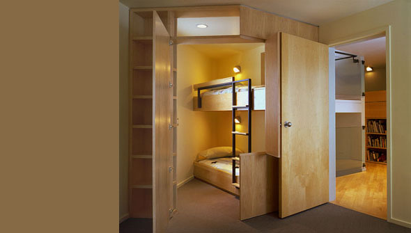 Bedroom with wooden bunk beds and built-in shelving adjacent to an open door reveals another room with bookshelves.