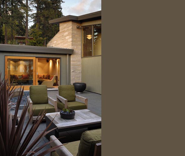 Patio seating area connected to an indoor living space in a courtyard house featuring wood and stone exterior materials.