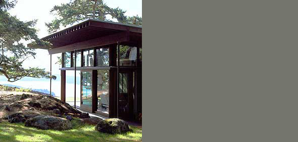 Partial view of a modern house with floor-to-ceiling glazing and a flat roof in a natural coastal setting.