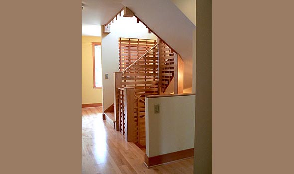 Wooden staircase with horizontal slat railing and wood flooring in a bright hallway.
