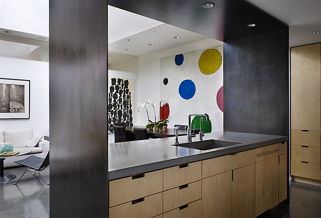 Kitchen interior featuring wood cabinetry, black countertop, and visible dining area with colorful dot artwork.