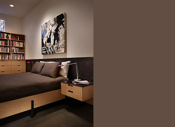 Bedroom interior featuring a wood-framed bed with black bedding and adjacent built-in bookshelves.