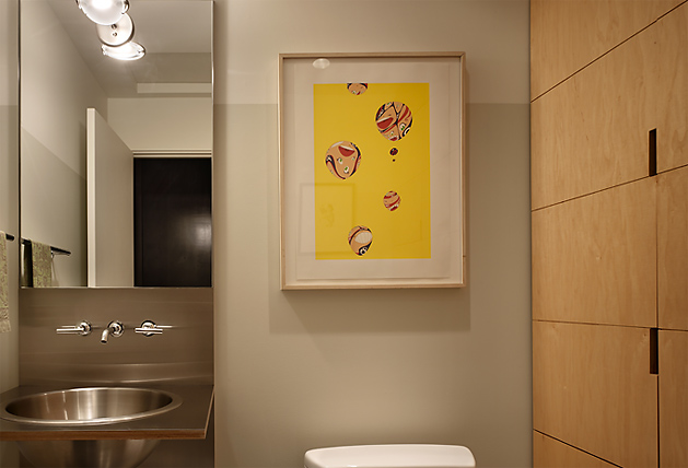 This bathroom features a stainless steel vessel sink, a large mirror, and wood-paneled wall with bright yellow artwork.