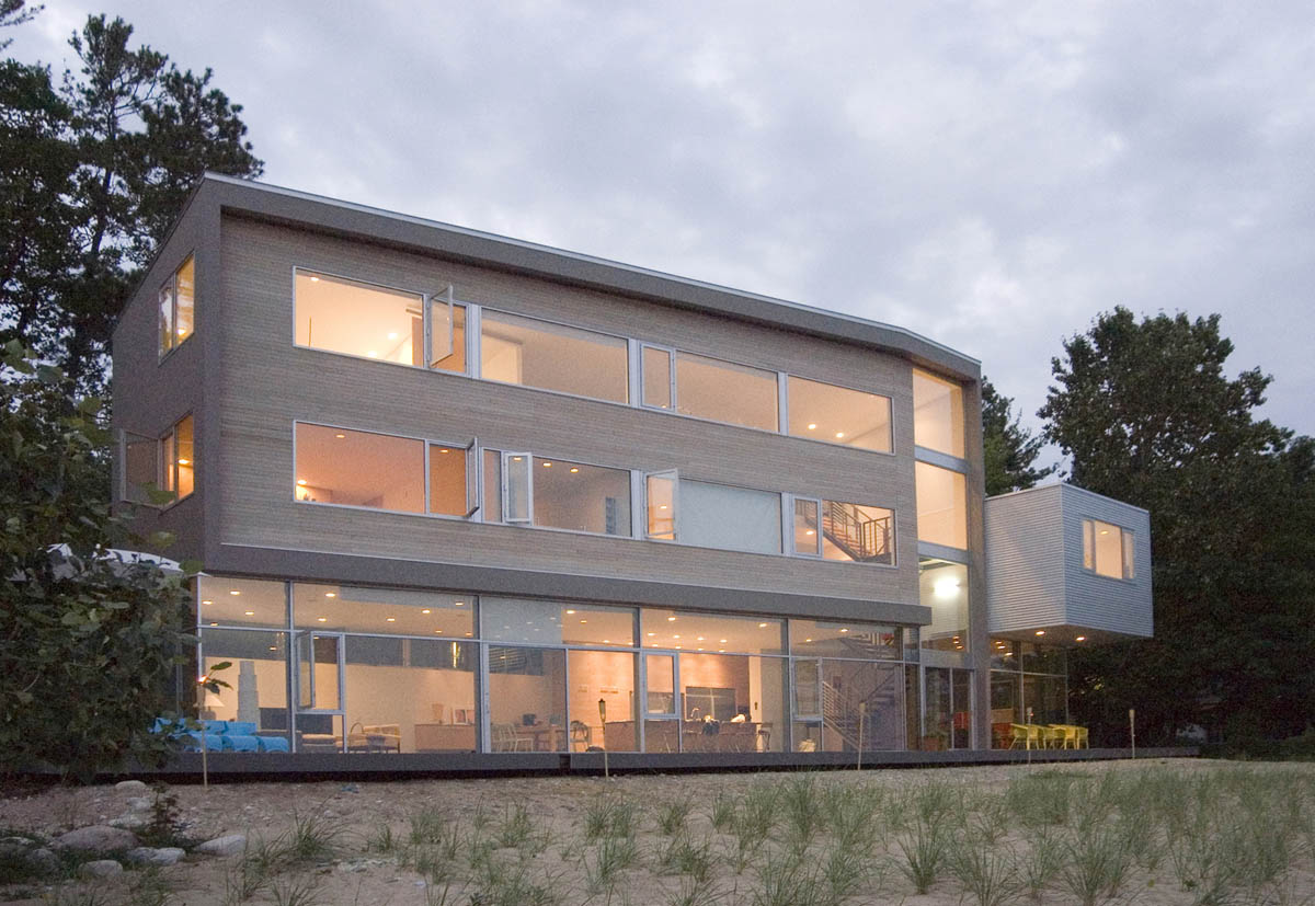 Three-story modern residence with extensive floor-to-ceiling glazing on the ground floor and horizontal window bands above.