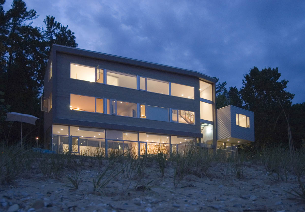 Three-story modern residence featuring extensive horizontal windows, photographed at dusk.