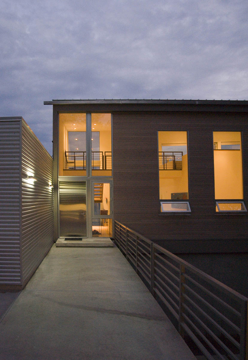 Entryway of a modern residence with large vertical windows and metal railing at dusk.