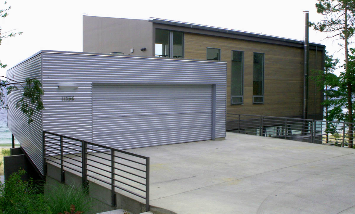 Exterior front view of a modern residence featuring a metal-clad garage and wood-paneled upper floor.