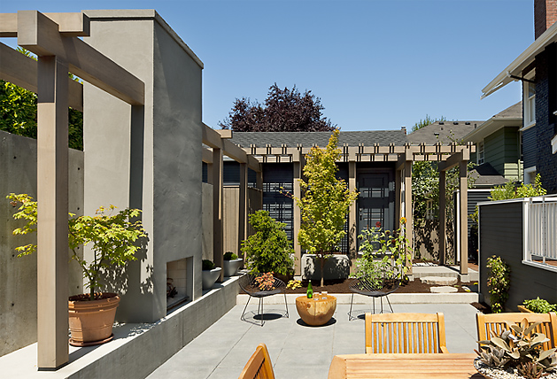 Mt Baker Courtyard features a concrete patio, wooden pergola, and outdoor fireplace surrounded by potted plants and seating.
