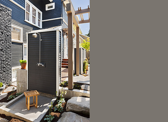 Courtyard outdoor shower with black shingle siding and a wooden pergola overhead.