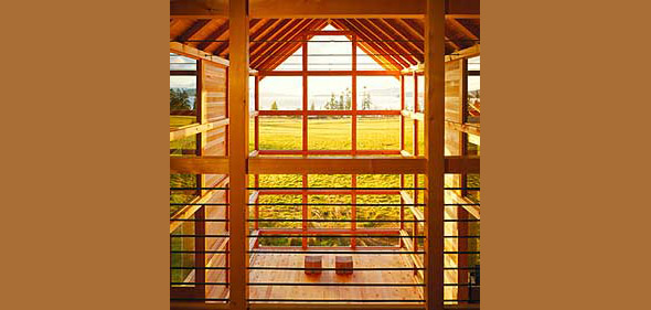 Wood-paneled interior features large window walls and exposed beams, highlighting timber joinery and metal bolts in a forest setting.