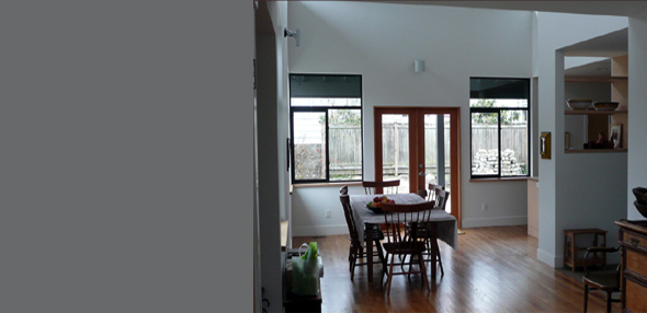 Dining area with wooden furniture and floor, white walls, and black-framed windows near a doorway.