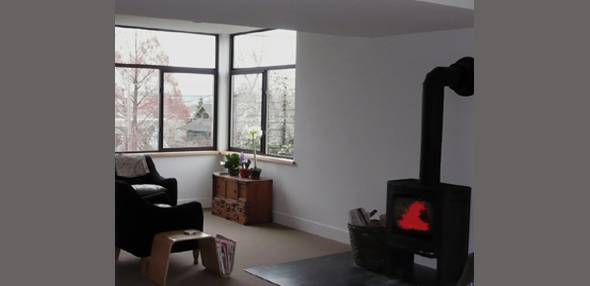 The living room features black window frames and a wood stove with a fire burning inside.
