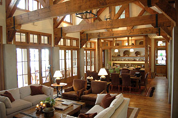 Open living and dining area with exposed wooden beams and multiple-pane windows.