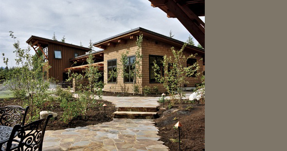 Mountain Meadow House features shingle siding, a sloped roof, and a landscaped courtyard with a stone pathway and pergola.