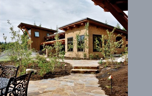 Mountain Meadow House features two wood-clad buildings connected by a stone pathway and young landscaping in a courtyard setting.