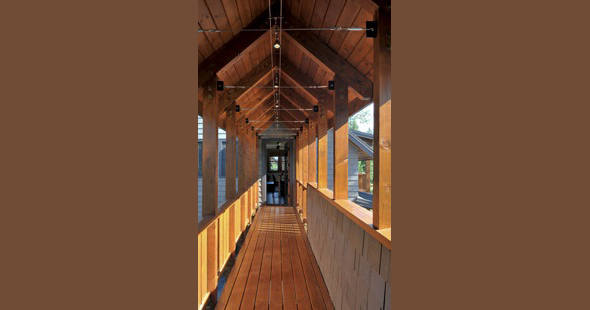 Covered wooden balcony hallway with vaulted ceiling and stone wall base at Mountain Retreat by Clinkston Brunner Architects.