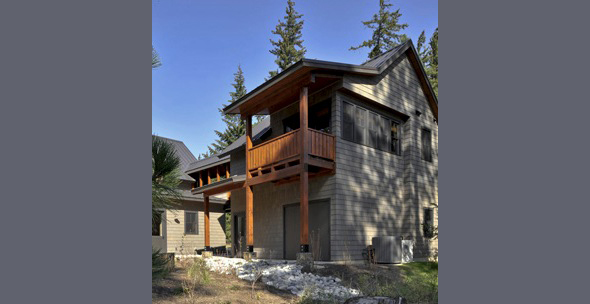 Two-story home with wood shingle siding, a covered balcony, and a gable roof in a wooded setting.