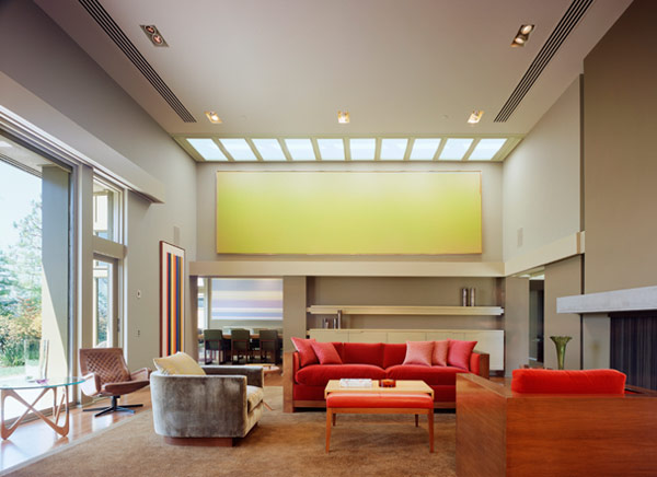 Living room with skylight ceiling, red couches, and an adjacent dining room in English House by CHU+GOODING Architects.