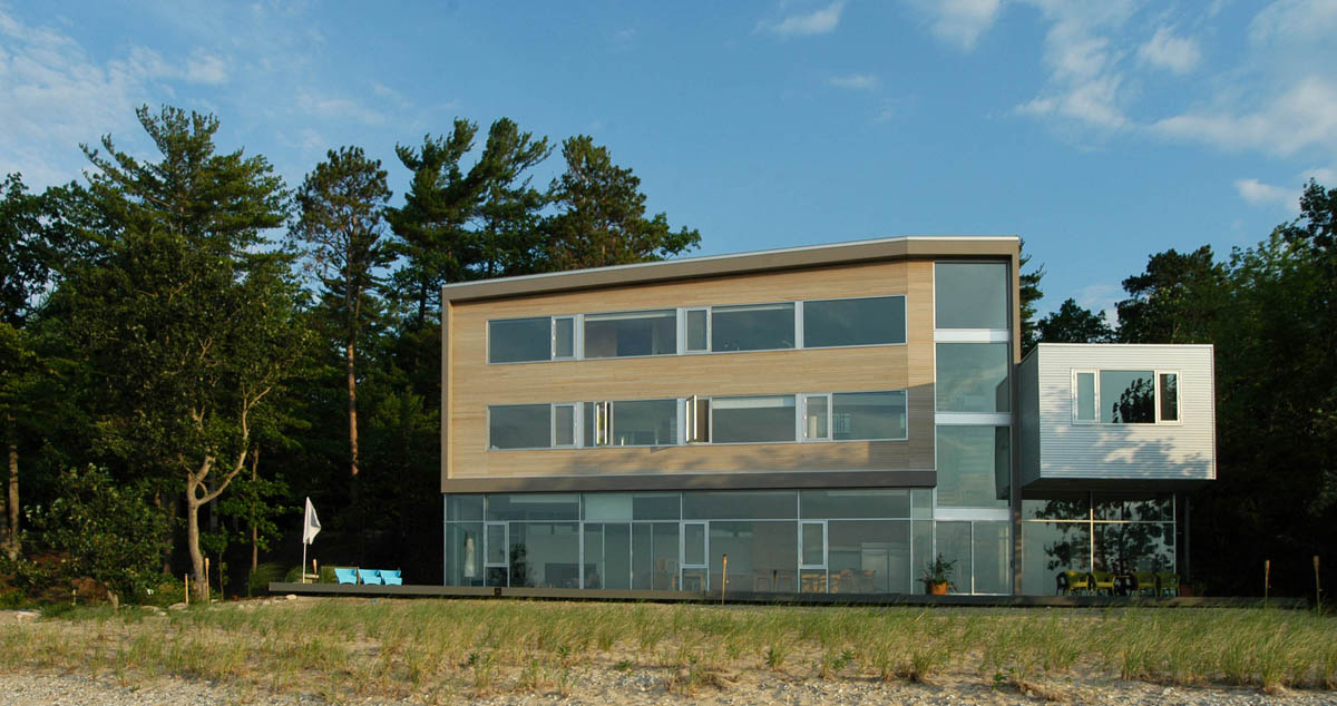 Modern three-story Michigan Residence features a flat roof, large windows, wood and composite siding, and a cantilevered section.