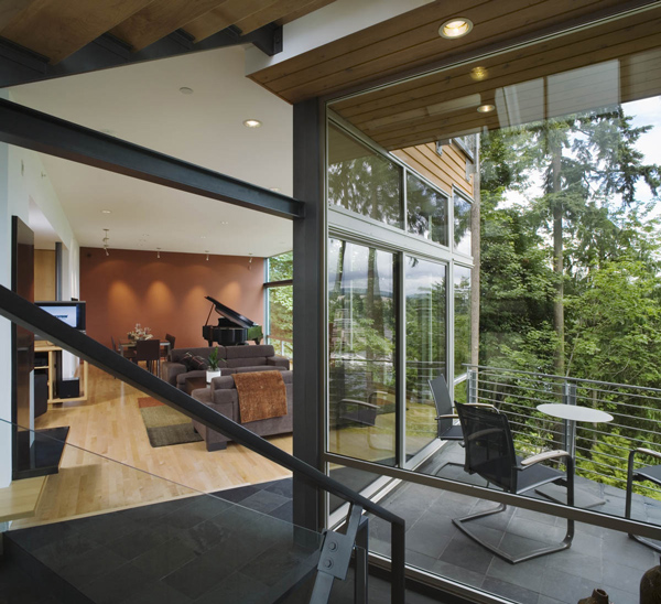 Interior view of a modern residence featuring a living room with piano and an outdoor covered patio with seating connected by sliding glass doors.