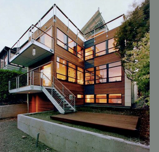 Wood-clad multi-story house featuring large window grids and metal railings on balconies and stairs.