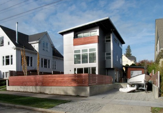 Three-story modern residence featuring large glass panels and wood siding with a flat roof and wood fenced front yard.
