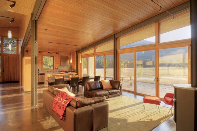 Living and dining area with floor-to-ceiling glazing and wood paneling looking out onto a mountain view.