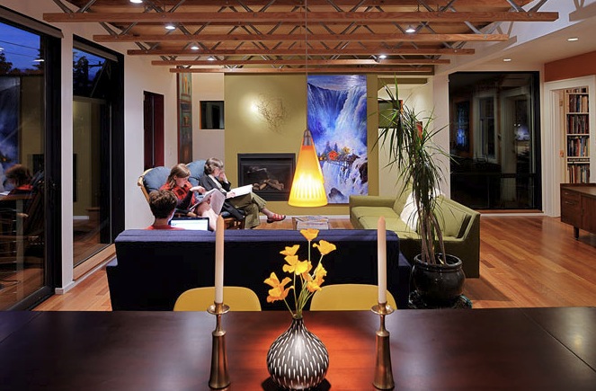 Living room in the Belyea-Faigin project features wooden trusses, a fireplace, and large windows with views outside.