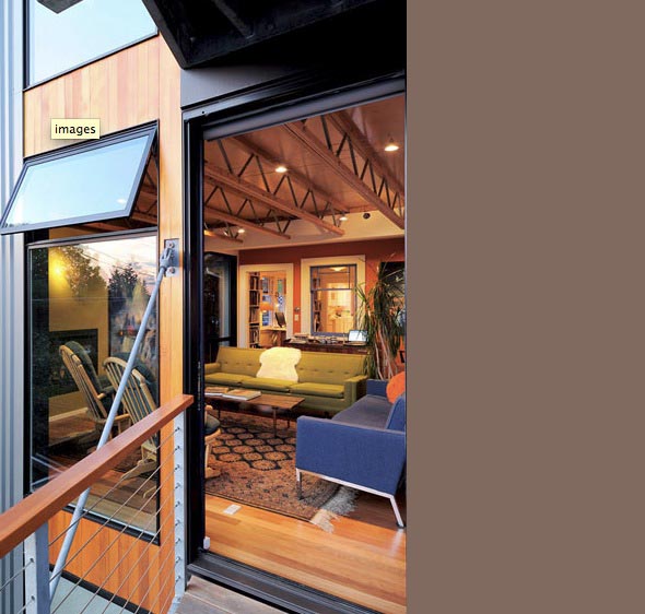 Living room with exposed wooden truss ceiling, mixed-color sofas, carpet floor, and large windows with metal cable railings outside.