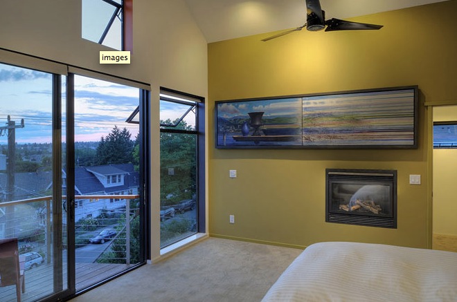 Bedroom with floor-to-ceiling corner windows and a gas fireplace below a large framed artwork.