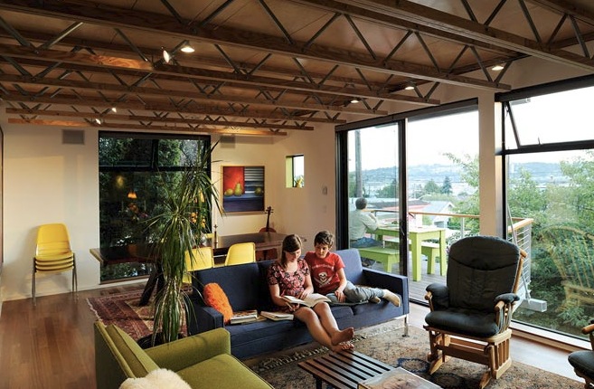 Living room with exposed wood beam ceiling, carpeted floor, and large glass sliding door to exterior deck with seating.