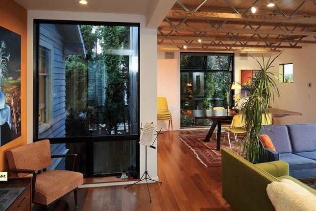 Interior of Belyea-Faigin house showing wooden truss ceiling, carpeted floor in dining area, and varied seating in living space.