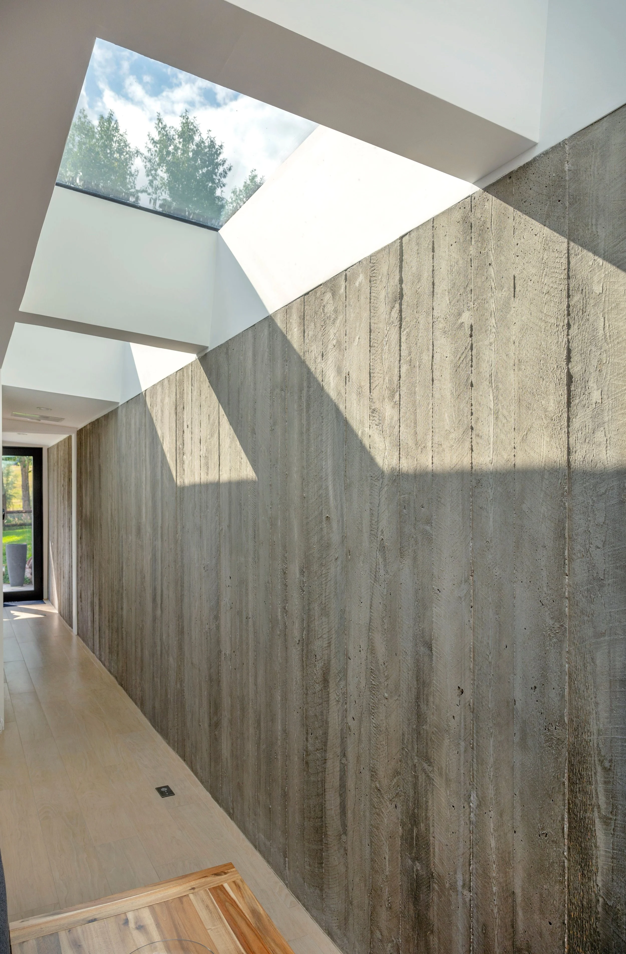 Interior hallway featuring a textured board-formed concrete wall under square skylights allowing natural light.