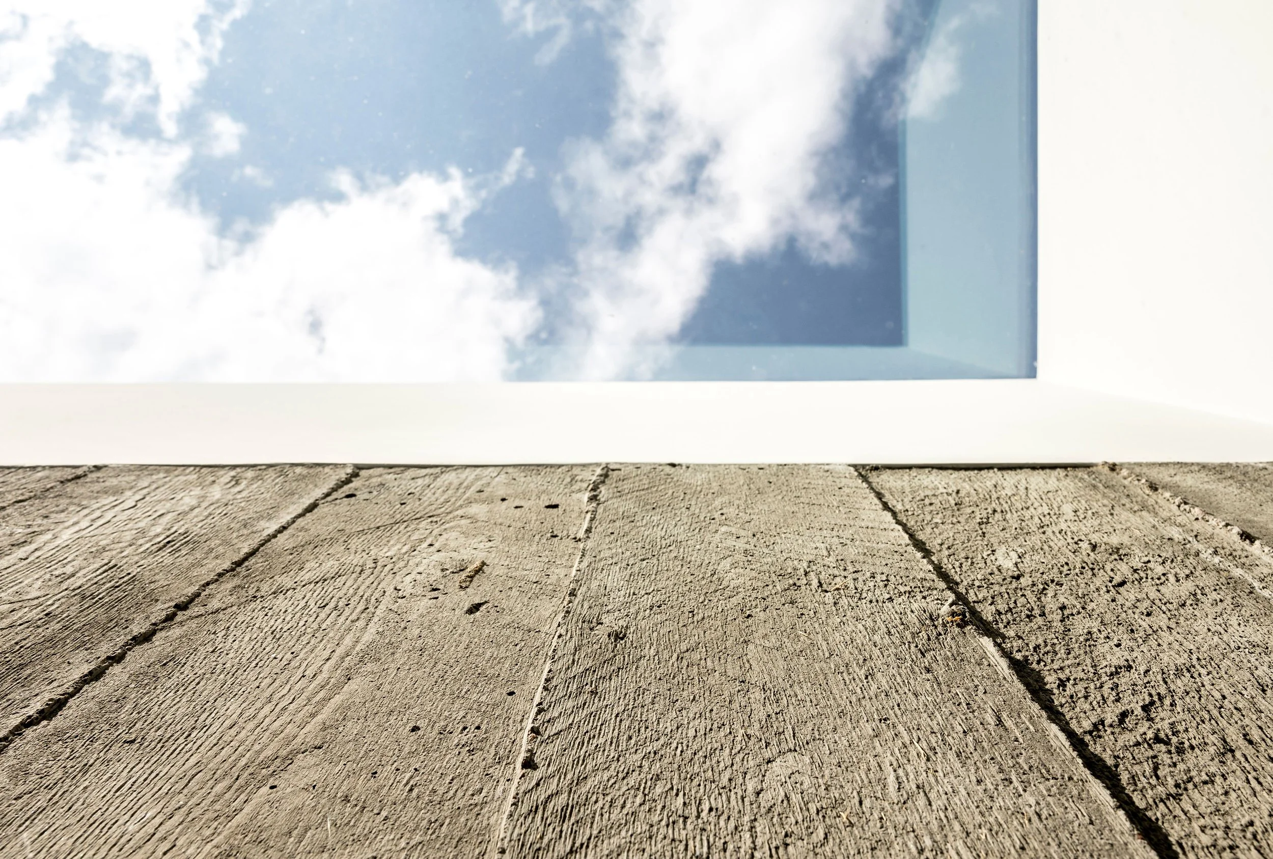 Square skylight set in a white ceiling above reclaimed wood planks with visible texture.