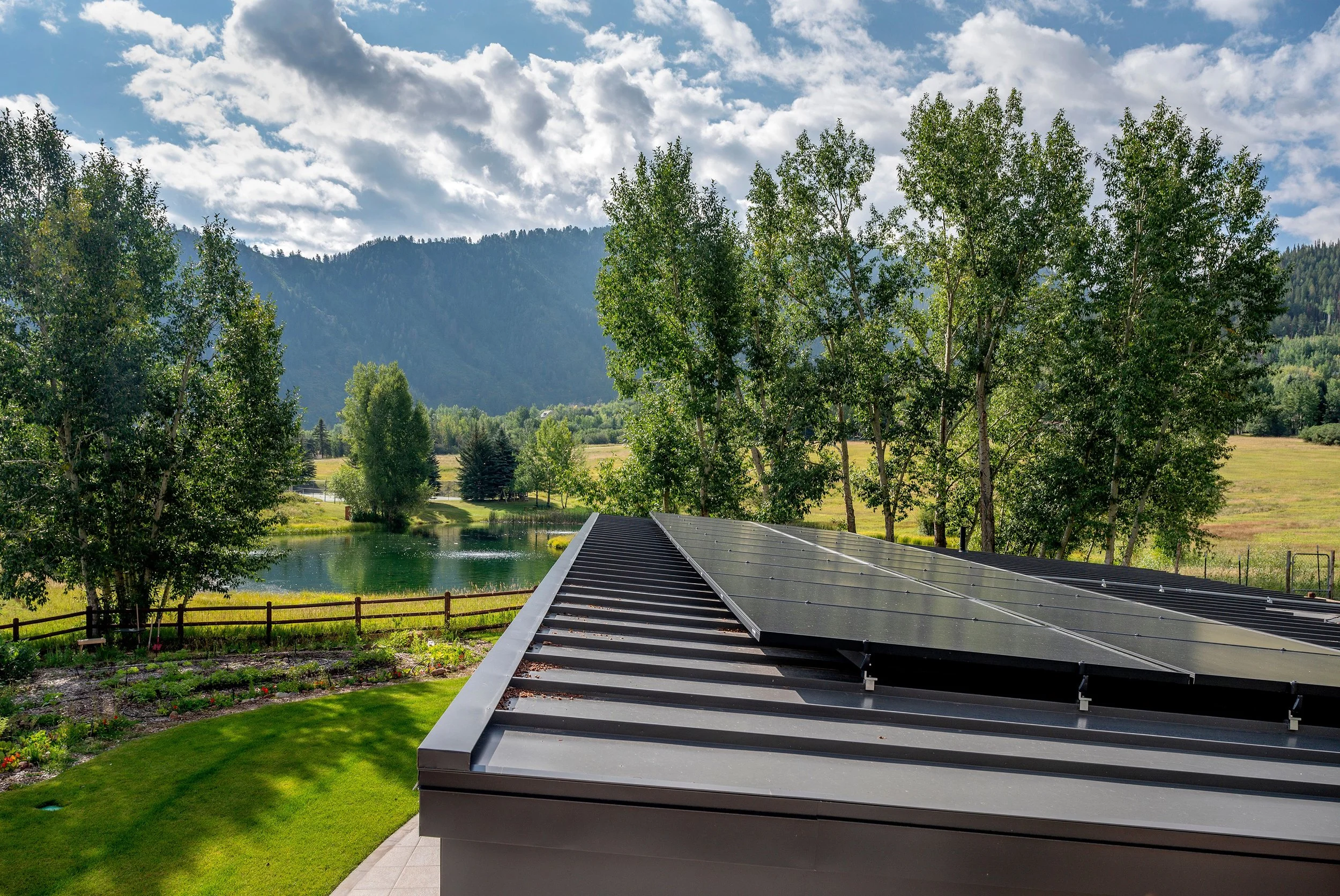 Flat roof with solar panels of the Meadowood Guesthouse overlooks a pond and mountains in Denver.