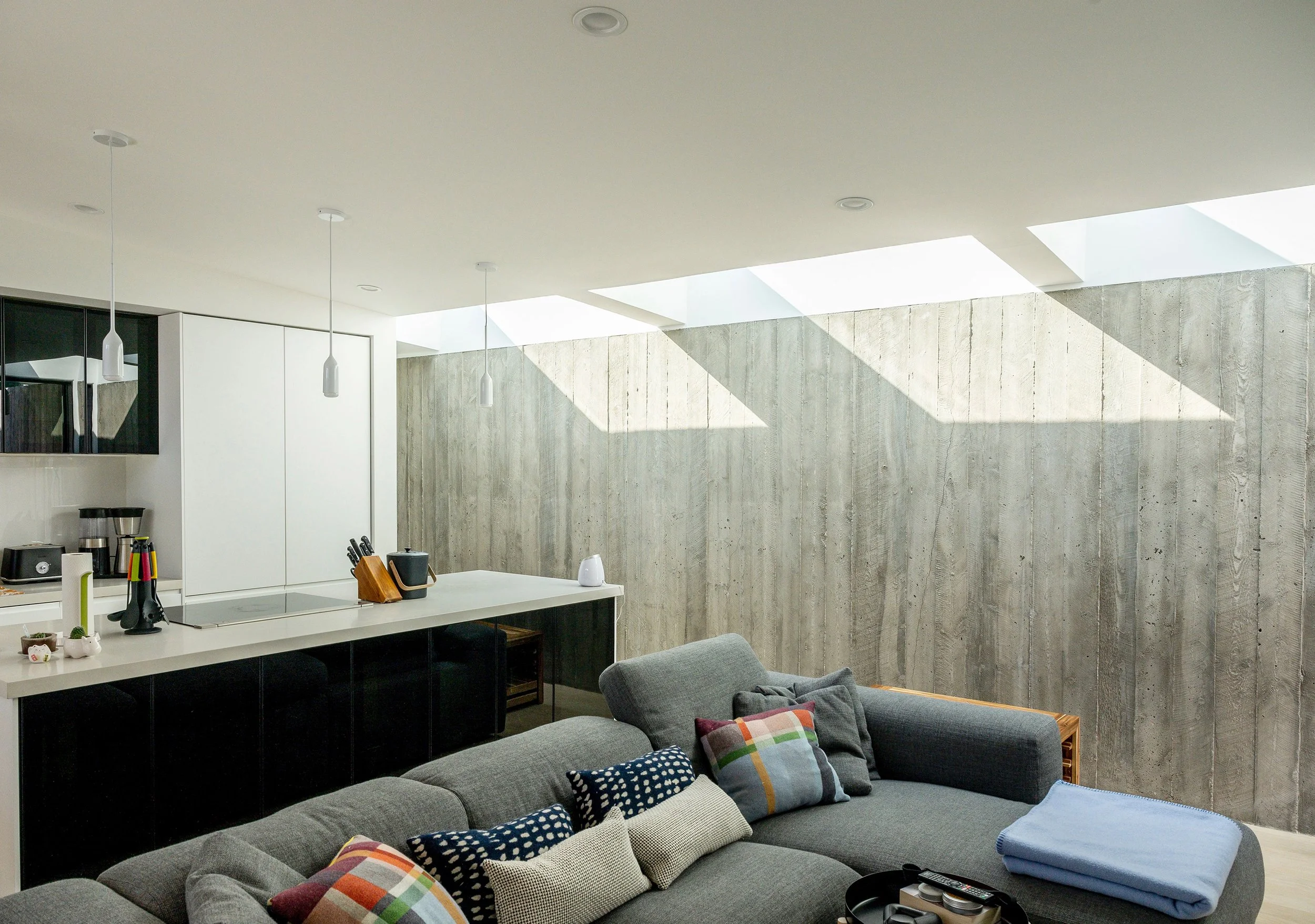 Meadowood Guesthouse interior features a kitchen and living area illuminated by square skylights and showcasing a textured concrete wall.