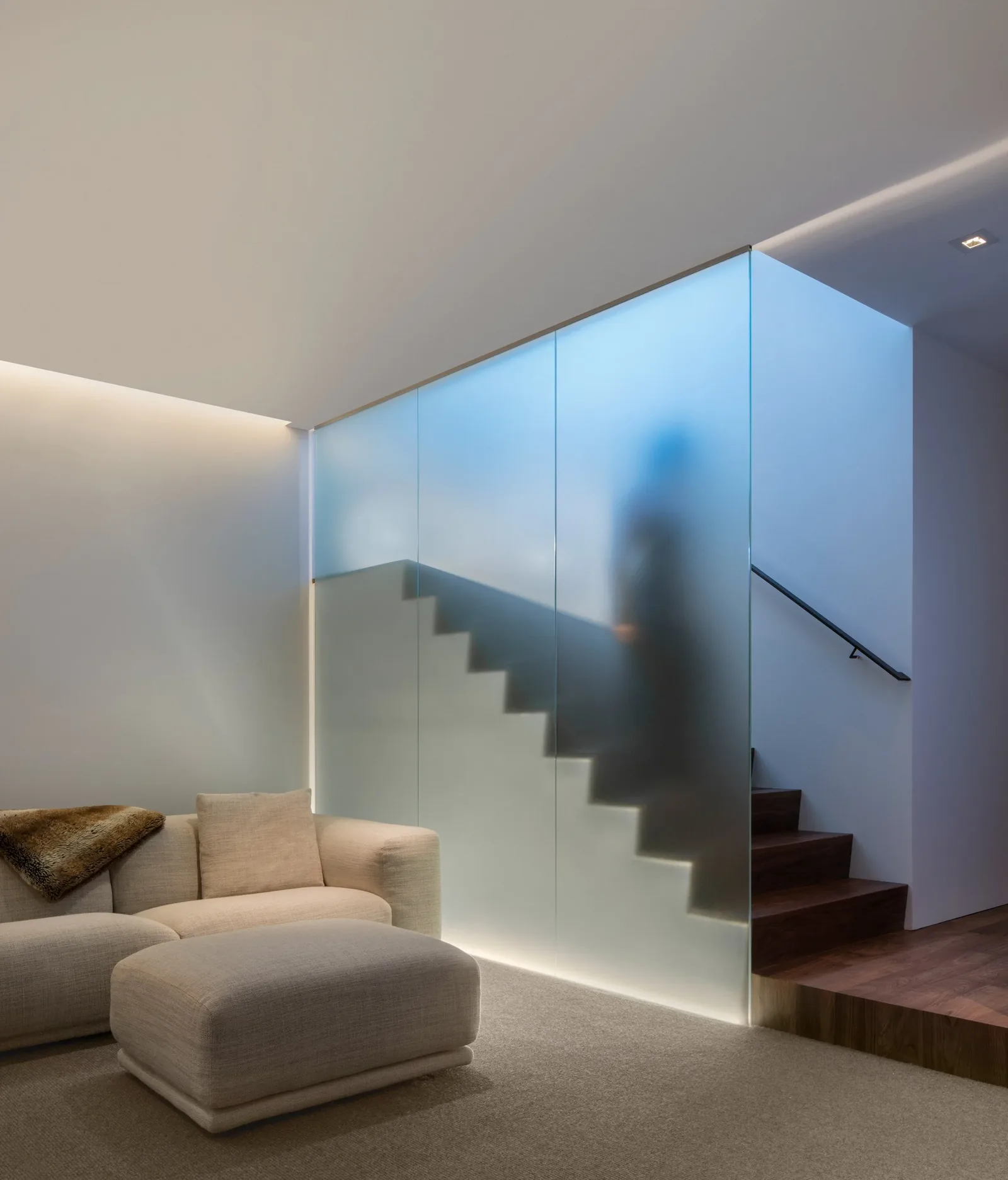Living room with beige seating adjacent to a staircase behind frosted glass panels.