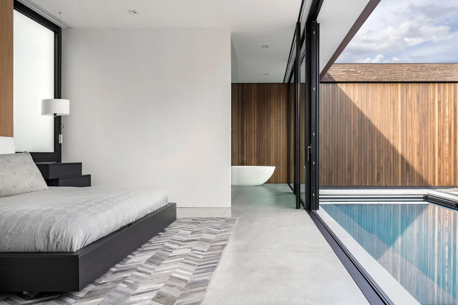 Bedroom with floor-to-ceiling sliding glass doors opening to a pool and a wood-paneled exterior wall.