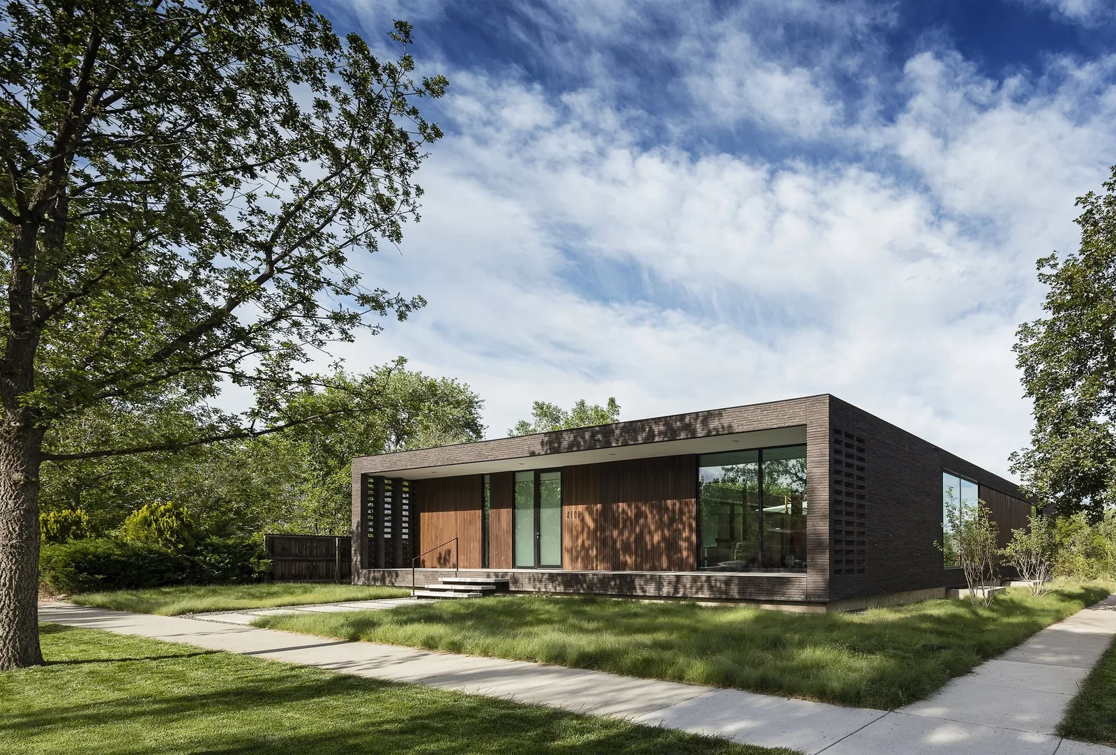Exterior front view of a single-story modern house featuring dark brick walls and large floor-to-ceiling windows.