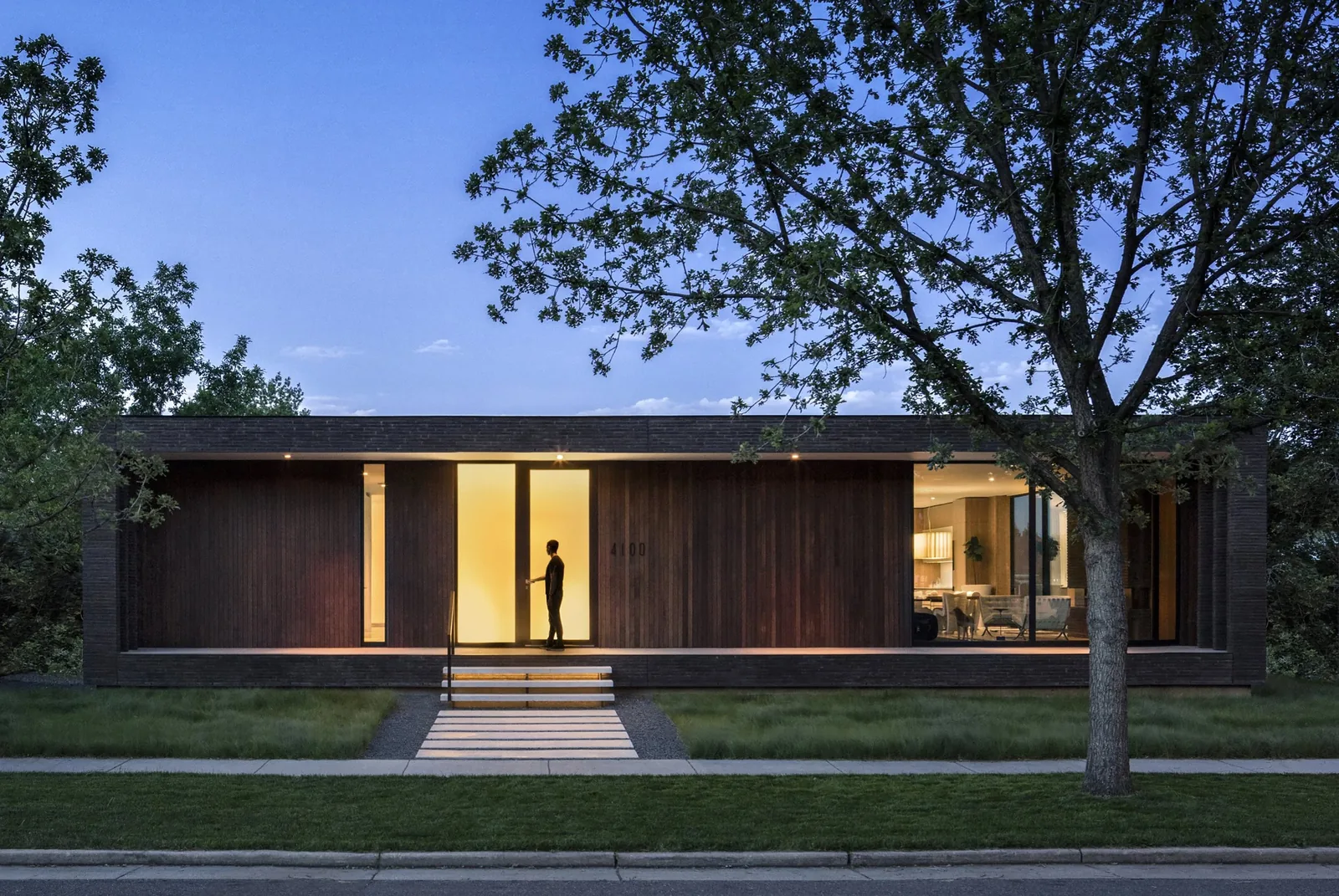 Dusk view of the Brick House showing the front facade with illuminated entry and integrated window walls.