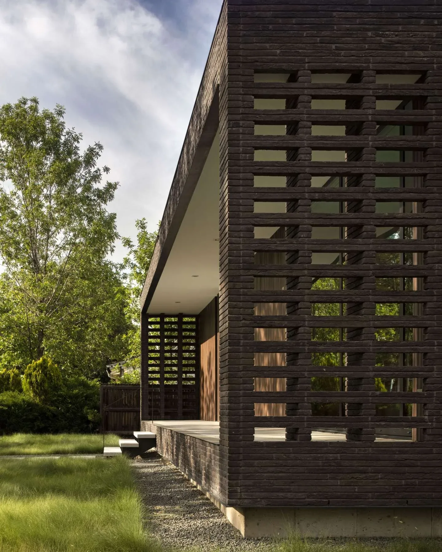 Side elevation of a house featuring a dark brick screen wall and a covered deck with steps.