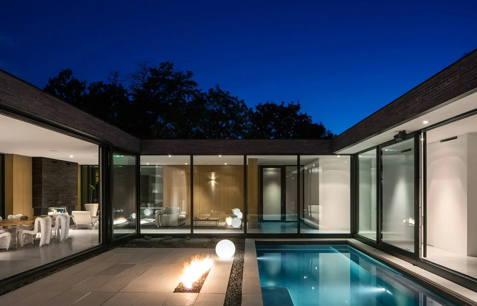 The modern Brick House features a U-shaped design with a courtyard containing a pool and a fire pit, visible at night.