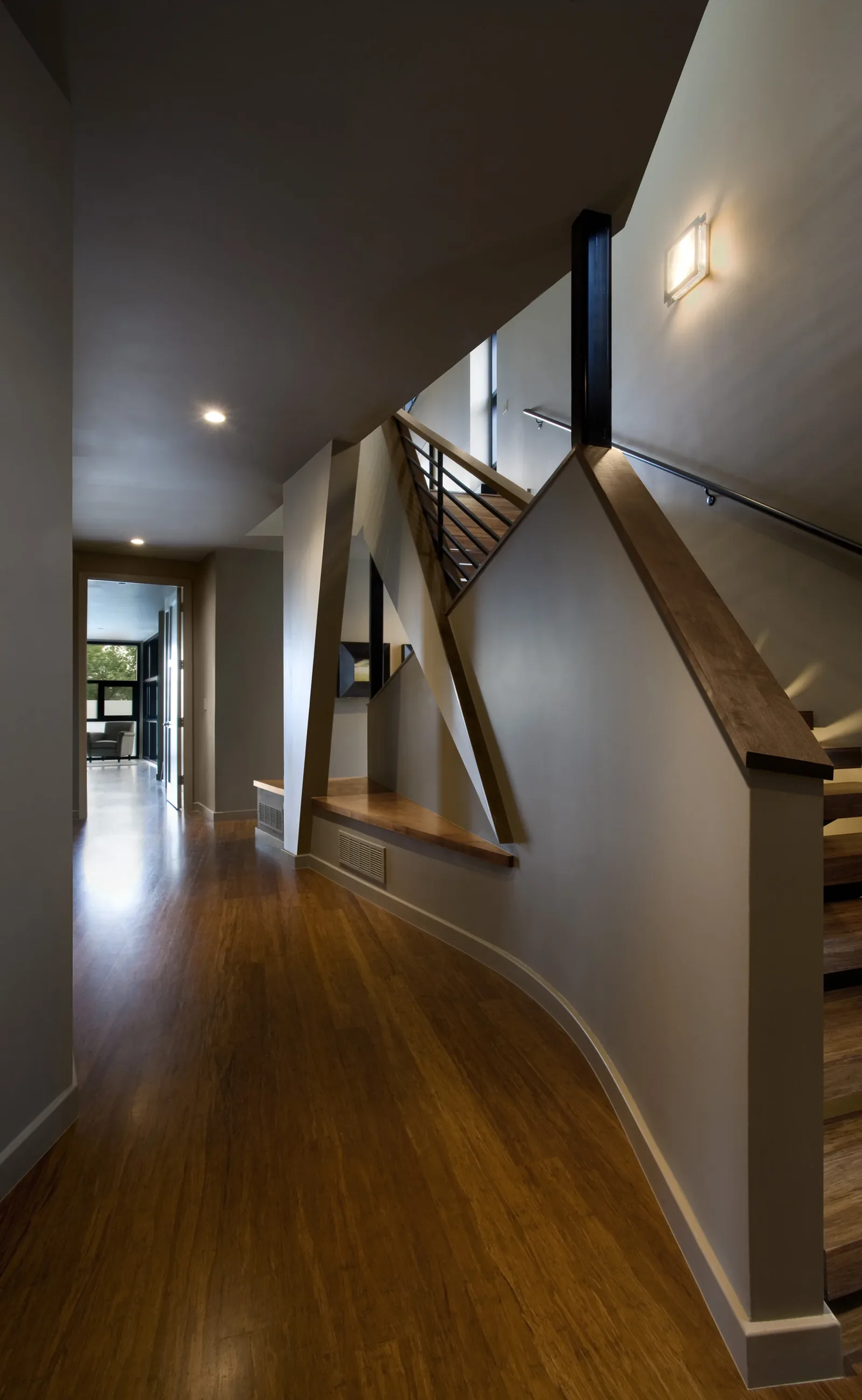 Curved hallway with a stair featuring wooden handrails and metal balusters along with a built-in bench below triangular wall supports.