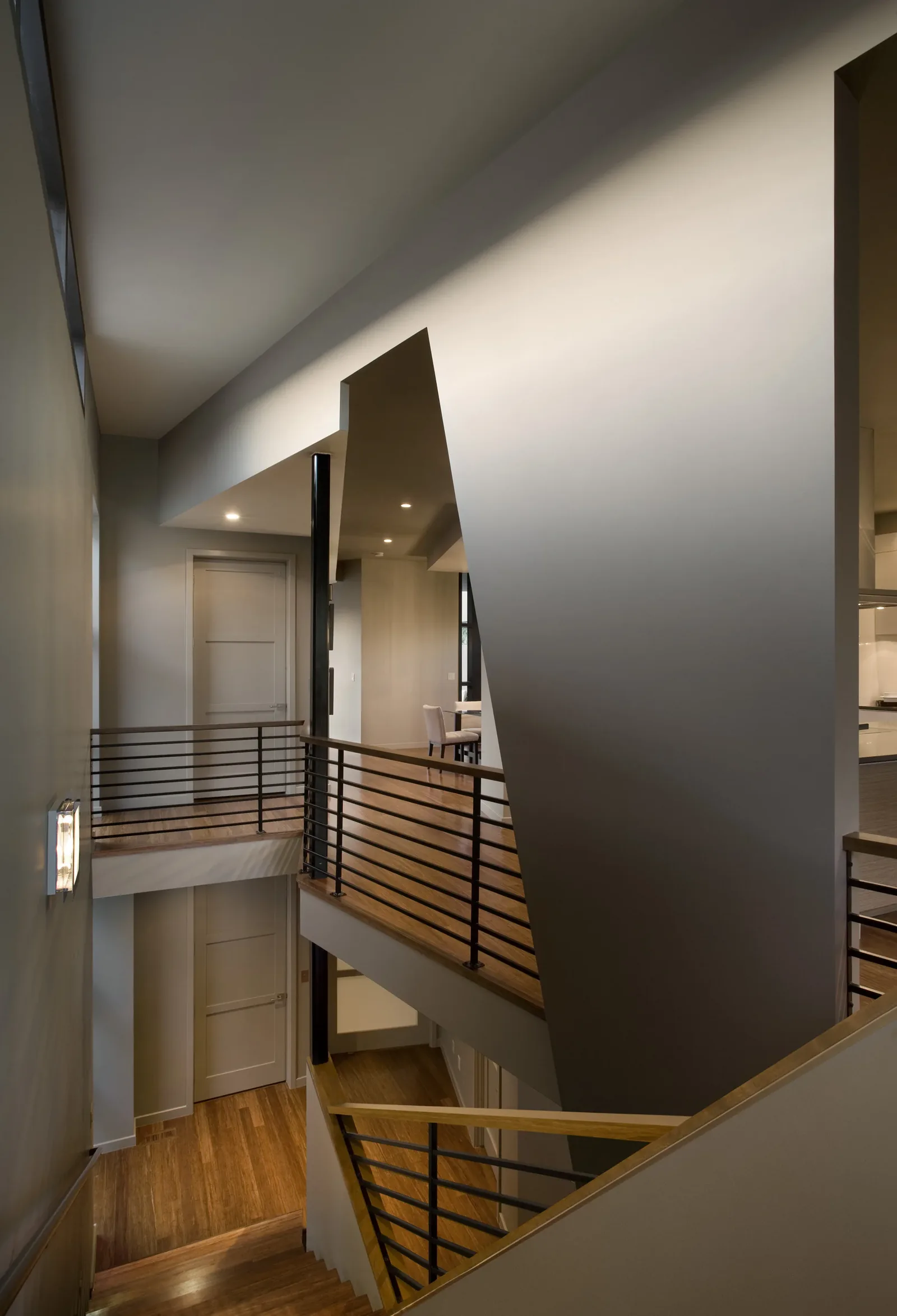 Two-story stairwell with wood flooring and black metal railings inside the Fractured Residence.